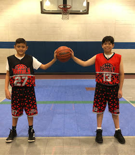 two kids each with one hand on a shared basketball standing in a gym